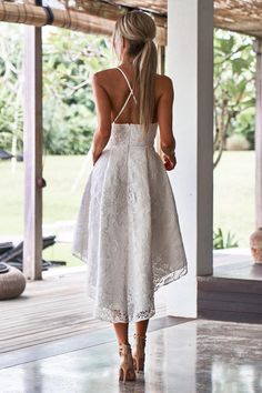 the back of a woman wearing a white dress and sandals, walking down a porch