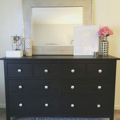 a black dresser with flowers and a mirror on top