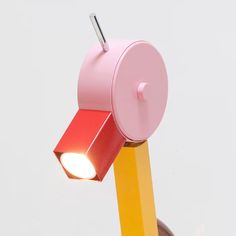 a pink and yellow lamp with a red light on it's side, against a white background