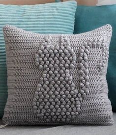 a crocheted pillow sitting on top of a bed next to two blue pillows