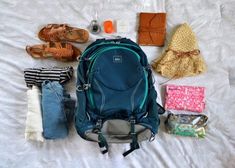 the contents of a blue backpack laid out on a white bed with shoes, wallets and other items