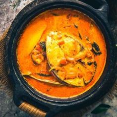 a bowl filled with curry and fish on top of a wooden table next to a spoon