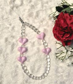 a pink and white necklace next to a red carnation flower on a white surface