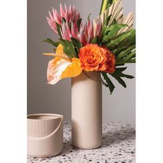 two vases with flowers in them sitting on a table next to a cup and container