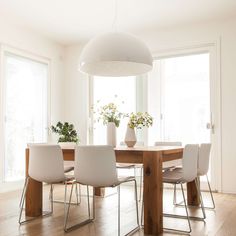 a dining room table with white chairs in front of large windows and wooden flooring