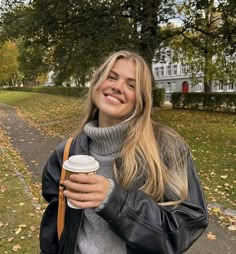 a woman is walking down the street with her coffee in her hand and smiling at the camera