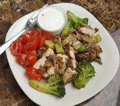 a white plate topped with meat and veggies next to a bowl of ranch dressing