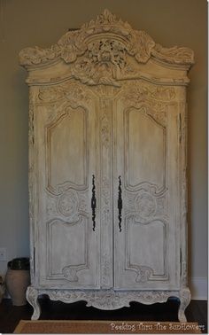 an old white armoire with ornate carvings on the top and bottom, sitting against a wall