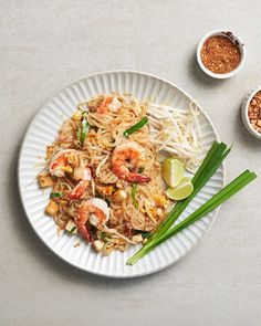 a white plate topped with noodles and shrimp next to two small bowls of seasoning