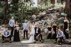 a group of people standing around each other in front of some rocks and trees with flowers