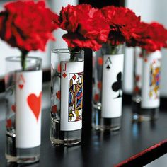 four vases with playing cards and red flowers in them are on a black table