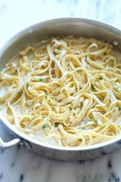 a pan filled with pasta and sauce on top of a marble counter