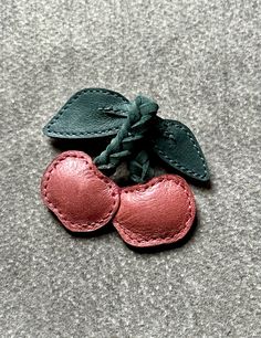 two leather hearts with leaves attached to them on a gray carpeted surface, one is pink and the other is green