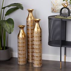 three gold vases sitting on top of a wooden floor next to a black chair