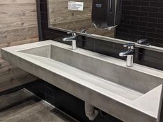 a bathroom sink with two faucets and a mirror above it in front of a wood paneled wall