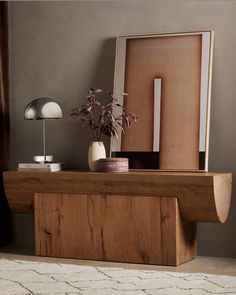 a wooden table topped with a vase filled with flowers next to a mirror and lamp