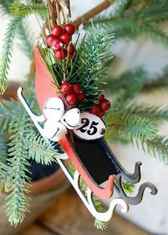 a christmas ornament hanging from a tree with red berries and pine cones on it