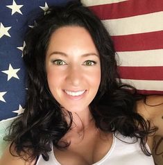 a woman laying on top of a bed next to an american flag and smiling at the camera