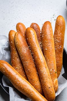 breadsticks in a black bowl on a white tablecloth with salt and pepper sprinkled on them