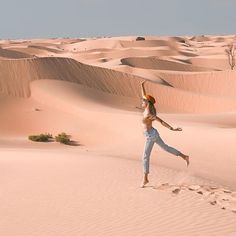 a woman standing in the middle of a desert with her arms up and legs spread out