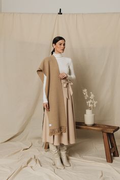 a woman standing in front of a white backdrop wearing a tan and beige blanket over her shoulders