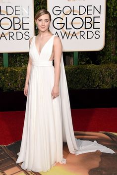 a woman in a white gown standing on a red carpet with her hands behind her back