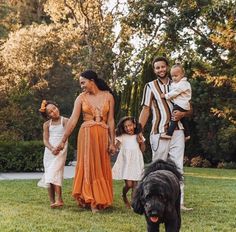 a family is walking in the grass with their dog and two children are holding hands