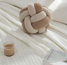 a brown and white knoted pillow sitting on top of a bed next to a cup of coffee