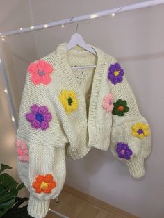 a white sweater with flowers on it hanging from a clothes rack next to a potted plant