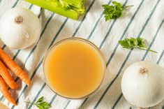 carrots, celery and onions on a towel next to a glass of orange juice