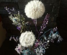 a vase filled with purple and white flowers on top of a table next to a brick wall