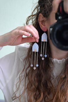 a woman is taking a photo with her camera and wearing some long white beaded earrings