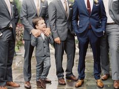 a group of men standing next to each other wearing suits and ties on a rainy day