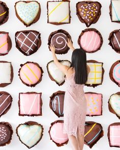 a woman standing in front of a wall made out of chocolate and pink heart shaped cookies