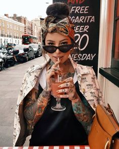 a woman sitting at a table with a drink in her hand and tattoos on her arm