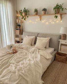 a bed with pillows, blankets and plants on the headboard is in front of a window