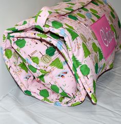 a pink and green duffel bag sitting on top of a white sheeted bed