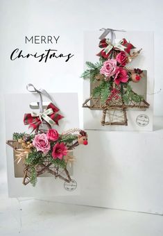 two christmas cards with pink and red flowers on them, hanging from the side of a white wall