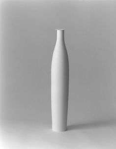 a white vase sitting on top of a table next to a gray wall and floor