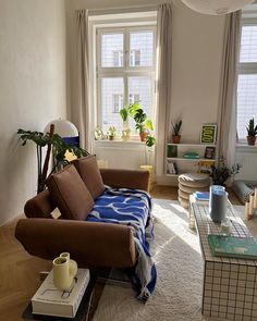 a living room filled with furniture and a large window covered in plants on top of a hard wood floor