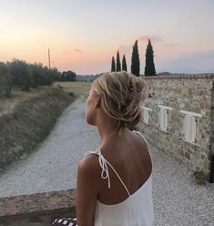 a woman standing in front of a stone building with trees on the other side of it