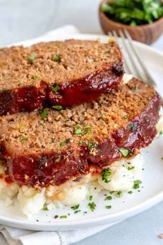 two slices of meatloaf with mashed potatoes and garnish on a white plate