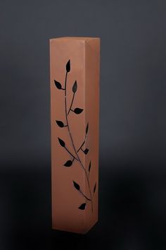 a brown vase with black leaves painted on the front and sides, against a dark background