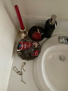 a bathroom sink that has various items on the counter next to it and a red candle