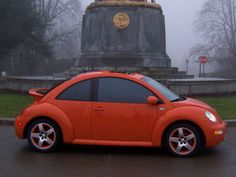 an orange car parked in front of a monument with a clock on it's face