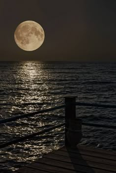 the full moon is seen over the ocean from a pier in front of some water