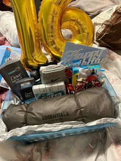 the contents of a birthday gift in a box on a bed with foil balloons and other items