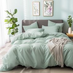 a bed with green sheets and pillows in a room next to a plant on the floor