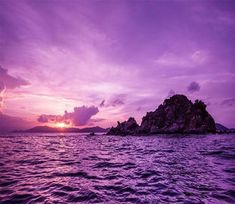 the sun is setting over an island in the ocean with purple hues and clouds