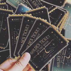 a hand is holding up some black and gold ticket stickers with stars on them